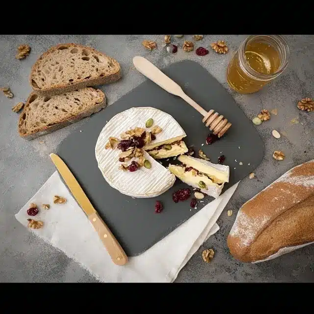 Recette de Camembert Farci aux Fruits Secs et Miel 2 Un camembert farci aux noix et aux cranberries, joliment présenté sur une ardoise avec du pain et du miel.