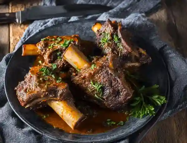 Souris d'Agneau Confite au Miel, Ail et Romarin : La Recette Fondante 2 Souris d'Agneau Confite au Miel et Romarin, tendre et brillante, servie sur une assiette rustique avec des herbes fraîches.